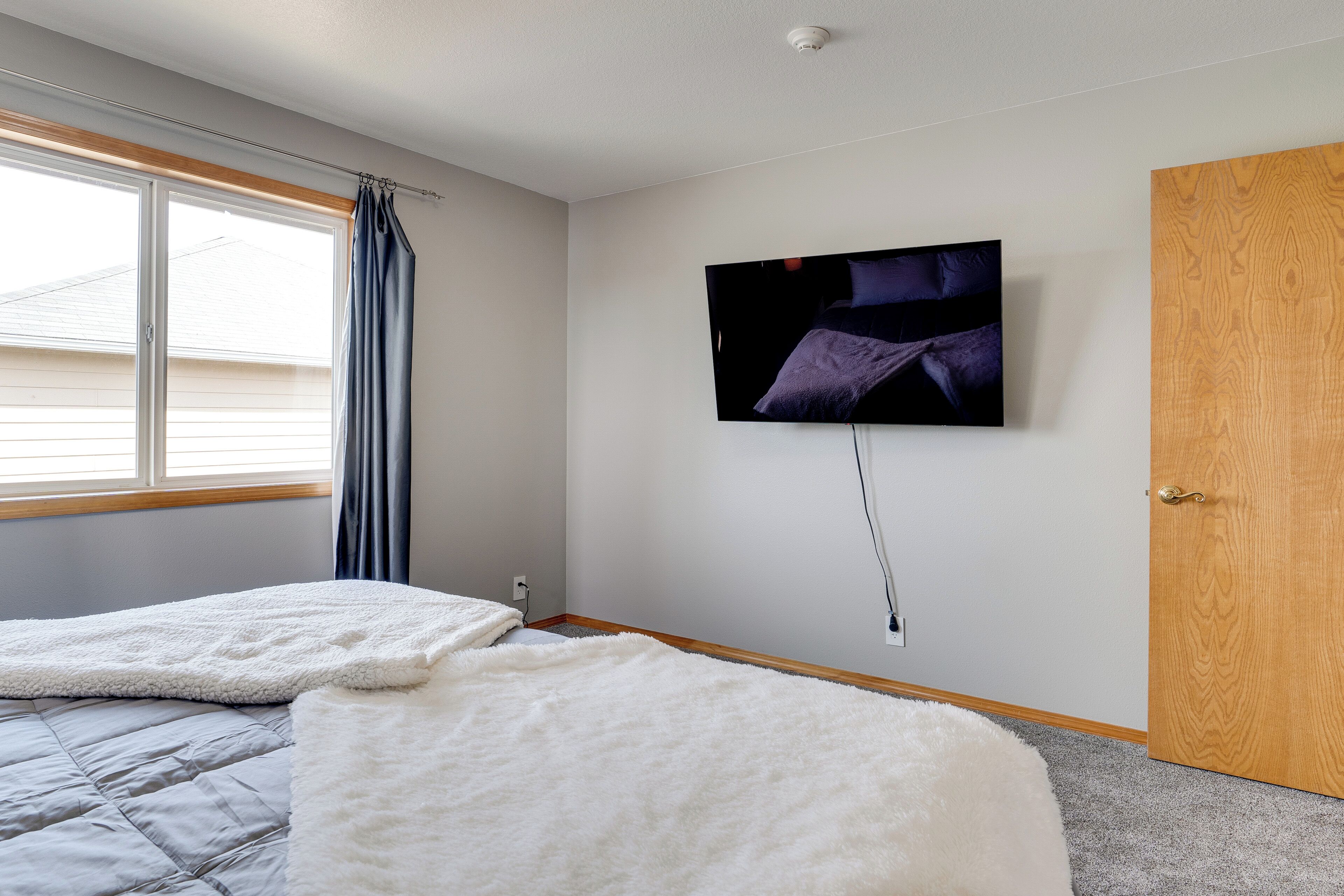 A bedroom with two beds, a TV mounted on the wall, and a wooden door.