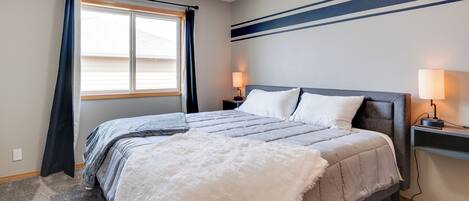 A neatly arranged bedroom with a large bed, two bedside tables with lamps, a window with curtains, and a wall with horizontal stripes.