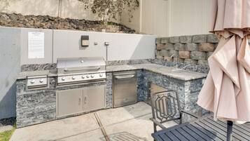 An outdoor kitchen with a grill, sink, and storage cabinets, set against a stone wall with a rock garden.