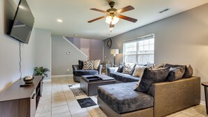 A modern living room with a flat-screen TV mounted on the wall, a ceiling fan, and a large window providing natural light. - Huntsville Vacation Rental < 5 Mi to Airport! (Huntsville)