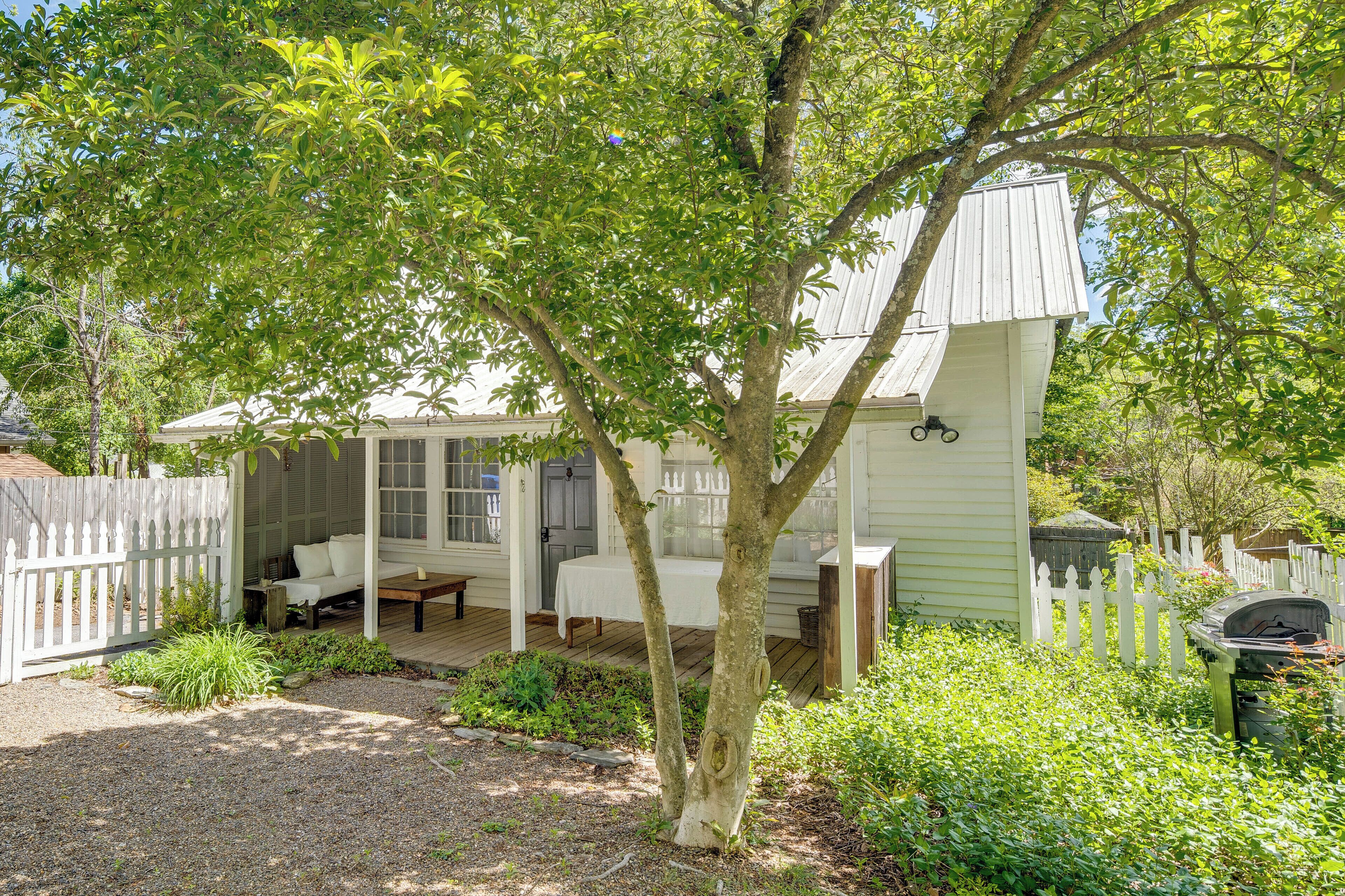 A white wooden house with a porch, a covered seating area, and a barbecue grill.