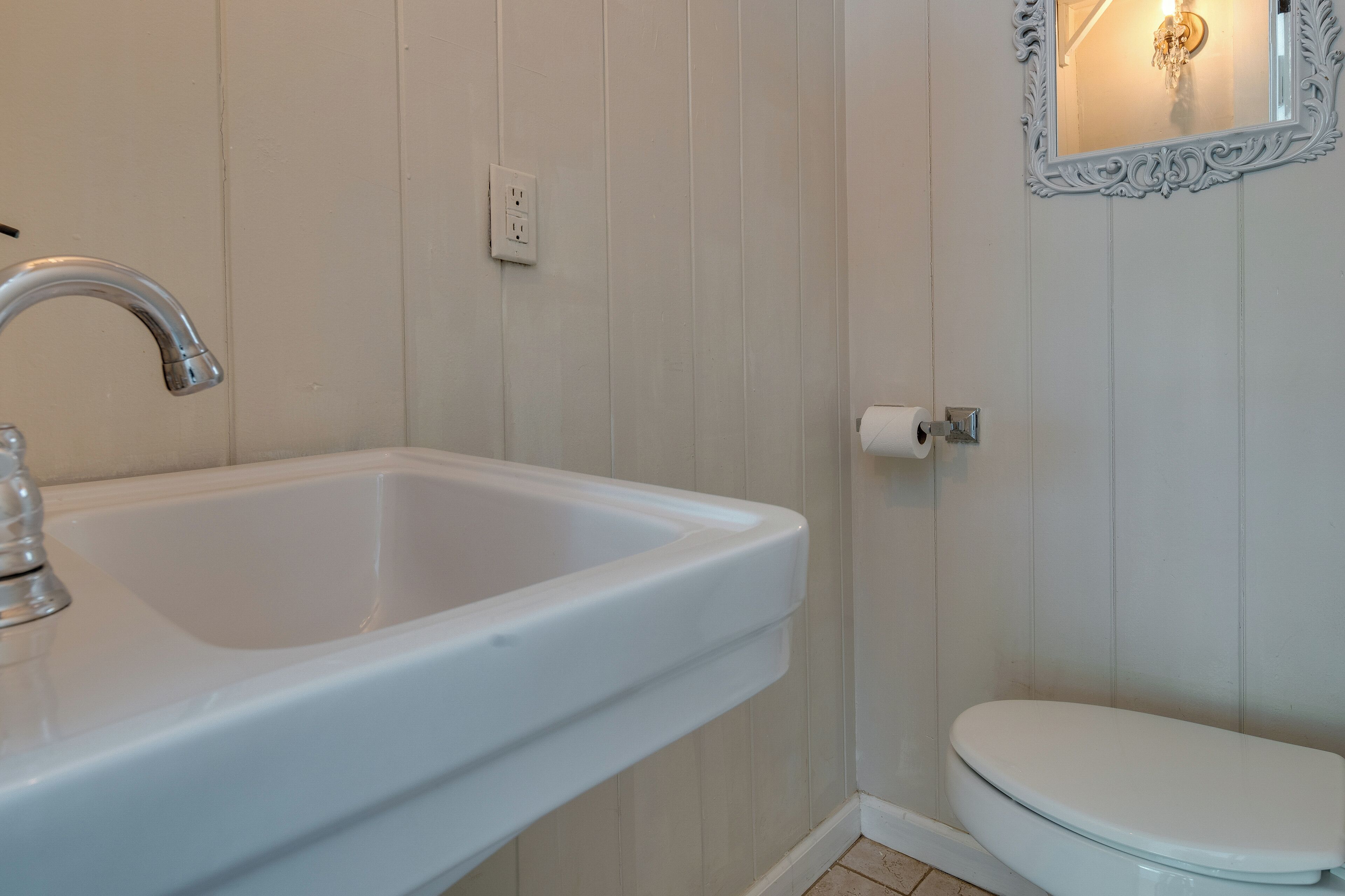 Un baño con un lavamanos blanco, un inodoro y un espejo con marco decorativo.