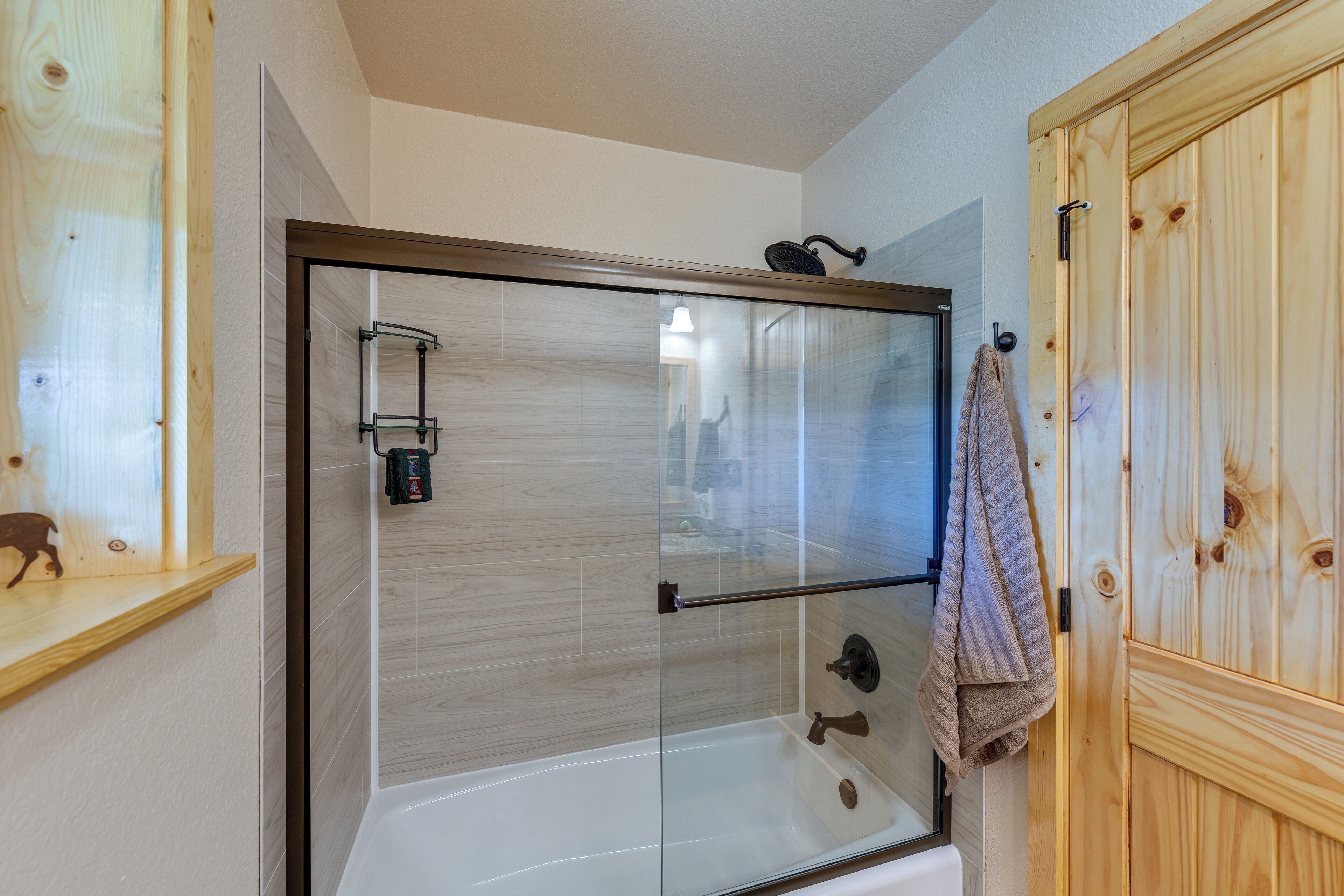 A glass-enclosed shower with a wooden door, a towel hanging on the door, and a wooden shelf with a decorative item.