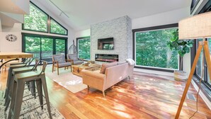 A modern living room with a stone fireplace, large windows, and a wooden floor. - 10 Mi to Nubs Nob: Modern Retreat w/ Fire Pit (Harbor Springs)