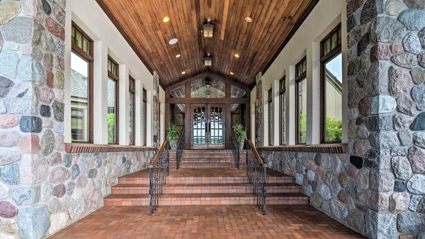 A stone-walled corridor with wooden beams, a brick floor, and a staircase leading to a door with glass panels. - 10 Mi to Nubs Nob: Modern Retreat w/ Fire Pit (Harbor Springs)