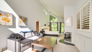 A modern living room with a sofa, coffee table, and artwork on the walls. - 10 Mi to Nubs Nob: Modern Retreat w/ Fire Pit (Harbor Springs)