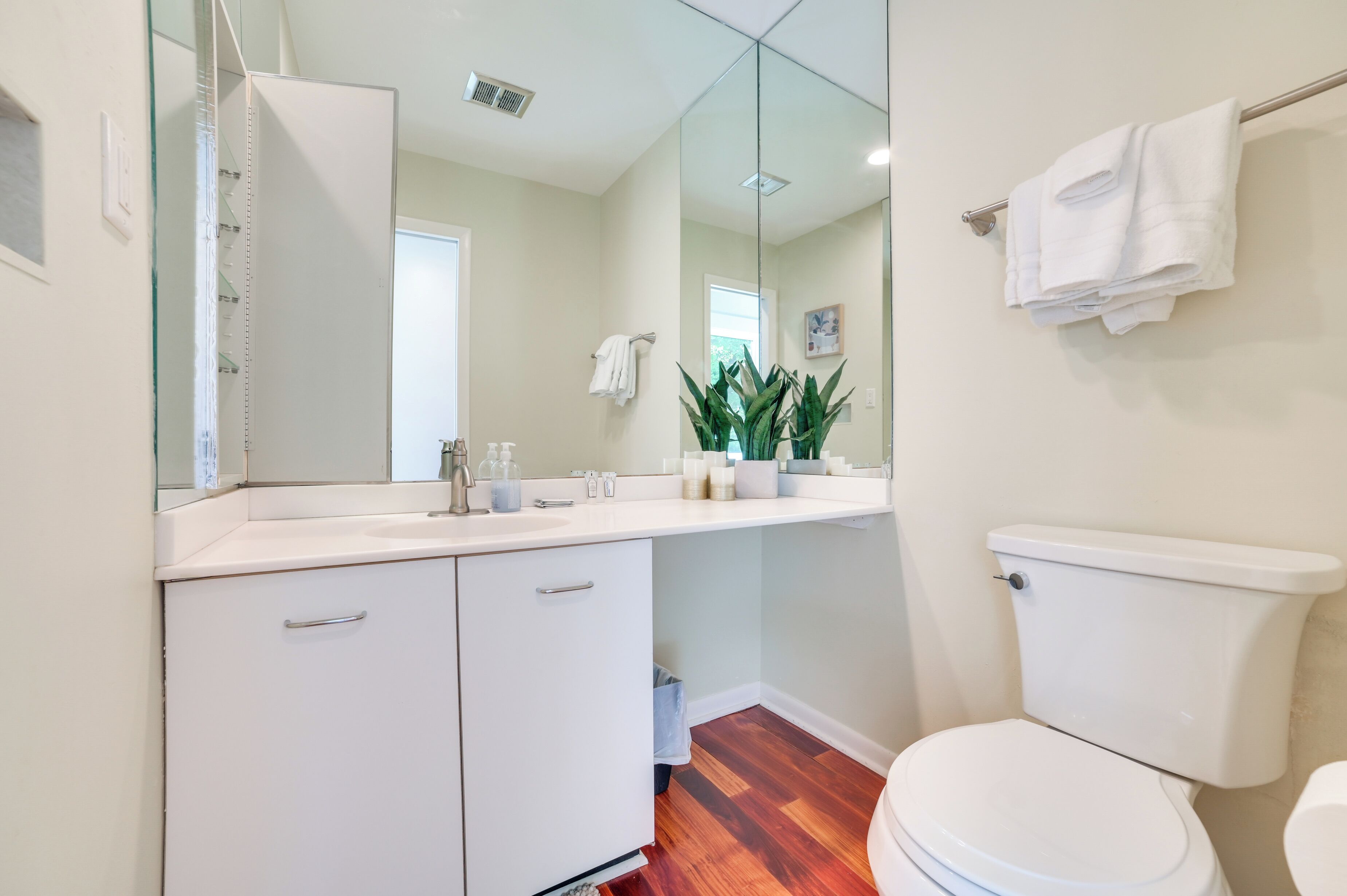 Un baño con inodoro blanco, lavabo con espejo y mueble bajo.