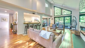 A spacious living area with a sofa, coffee table, and a hanging chair. A kitchen with a bar is visible in the background. - 10 Mi to Nubs Nob: Modern Retreat w/ Fire Pit (Harbor Springs)
