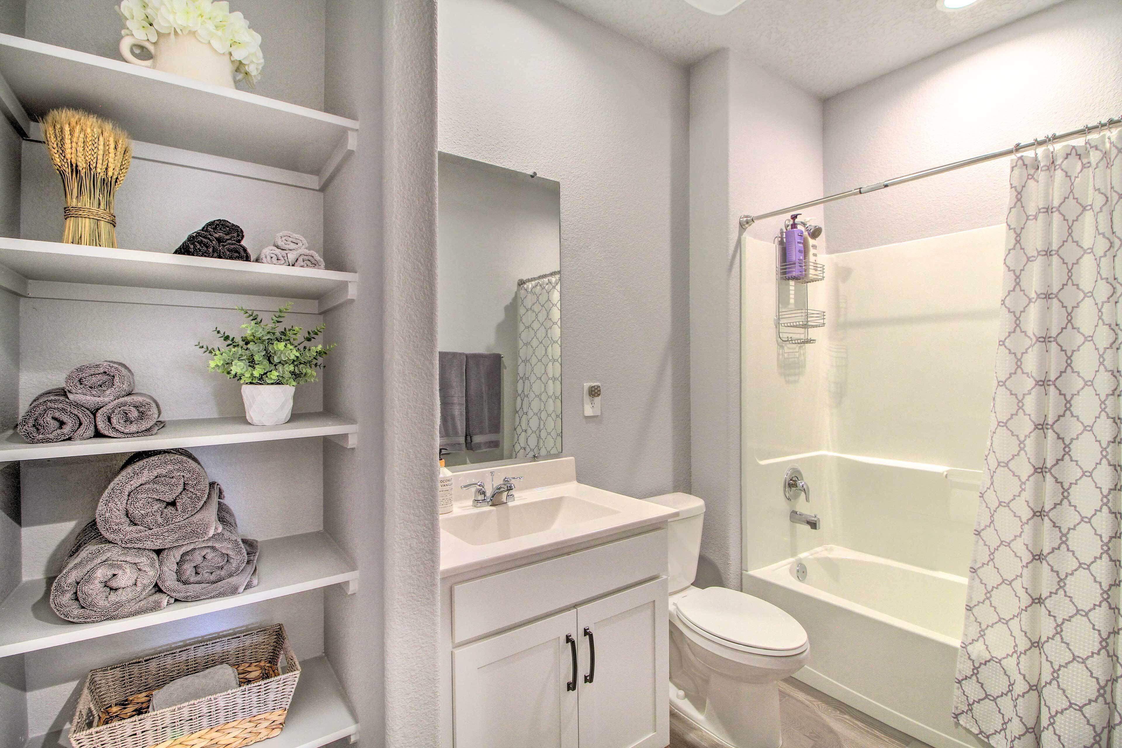A bathroom with a bathtub, toilet, and shelves with towels and toiletries.