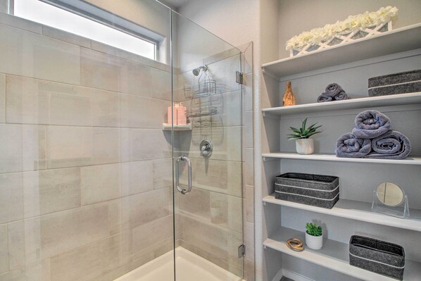 Une salle de bain moderne avec une douche à parois de verre, des murs carrelés et des étagères où sont rangés les articles de toilette et les serviettes.