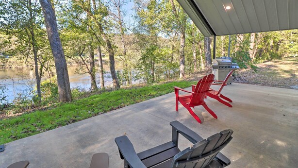 A covered patio with a view of a lake and trees, featuring two Adirondack chairs and a grill. - Riverfront 'heaven on the White' w/ Covered Patio! (Norfork)
