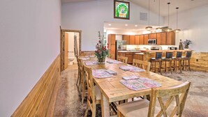 A spacious dining area with a wooden table set for six, a kitchen in the background, and a ceiling fan. - Riverfront 'heaven on the White' w/ Covered Patio! (Norfork)