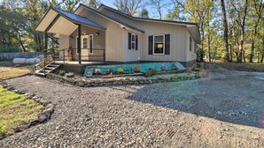 A single-story house with a covered porch, a small front yard with a gravel path, and a stone retaining wall. - Riverfront 'heaven on the White' w/ Covered Patio! (Norfork)