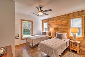 A bedroom with two beds, wooden walls, a ceiling fan, and large windows. - Riverfront 'heaven on the White' w/ Covered Patio! (Norfork)
