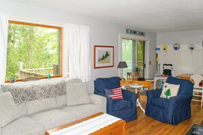 Un salon comprenant un canapé, deux fauteuils, une table et donnant sur l’extérieur.