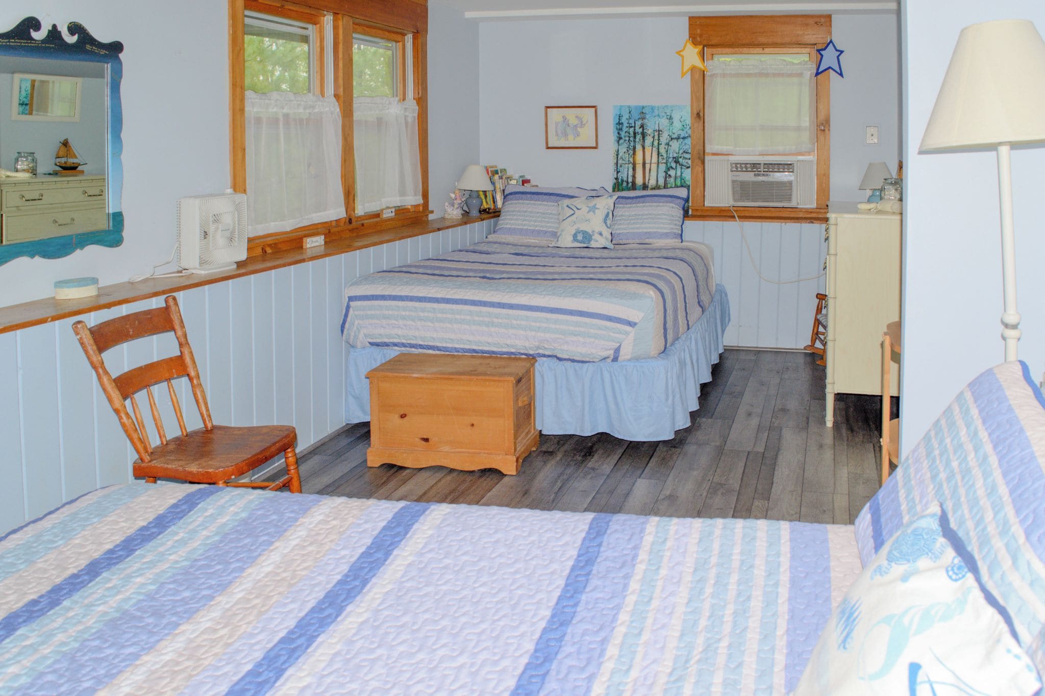 Een slaapkamer met een bed, een stoel, een nachtkastje, een dressoir en een raam met gordijnen.