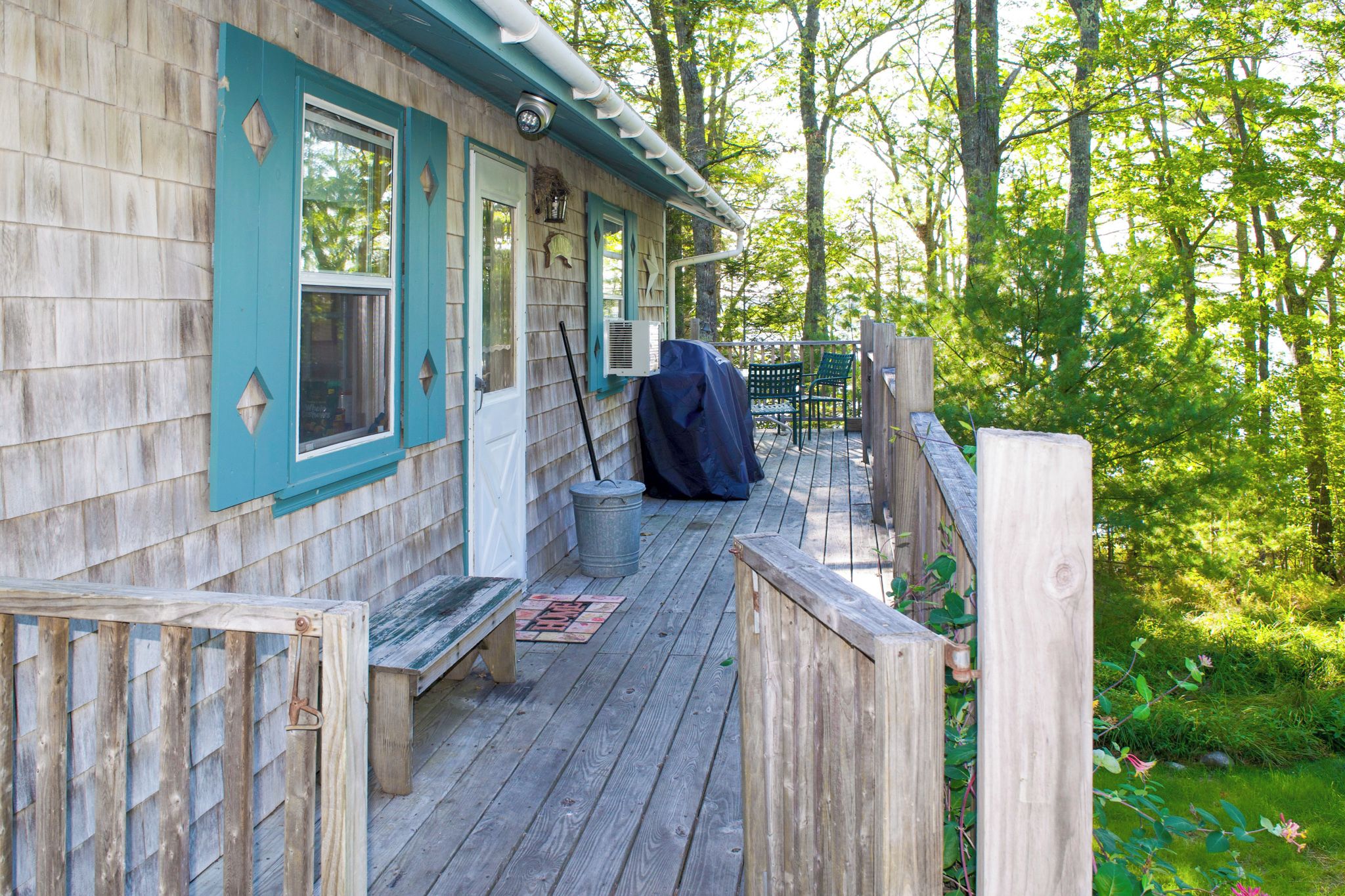 A wooden deck with a bench, a covered grill, and a metal trash can.