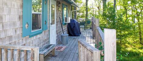 A wooden deck with a bench, a covered grill, and a metal trash can.