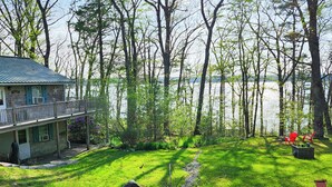A house with a deck overlooking a lake, surrounded by trees and grass. - Cozy Waterfront Cottage on Montsweag Bay! (Wiscasset)