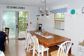 A dining area with a wooden table, white chairs, a chandelier, and a view through a sliding glass door to the outdoors.