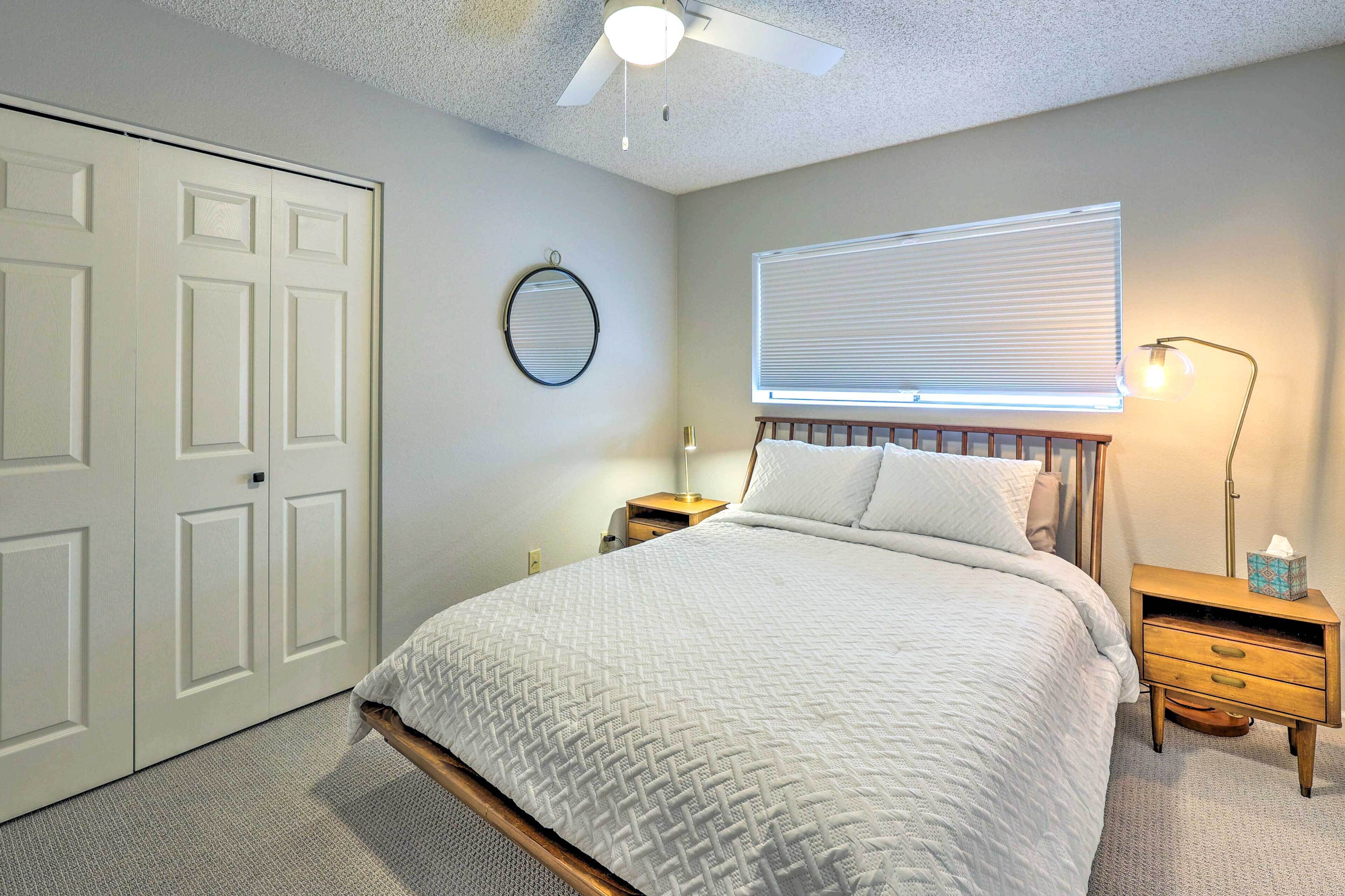 A bedroom with a bed, bedside tables, a ceiling fan, a window with blinds, and a door.