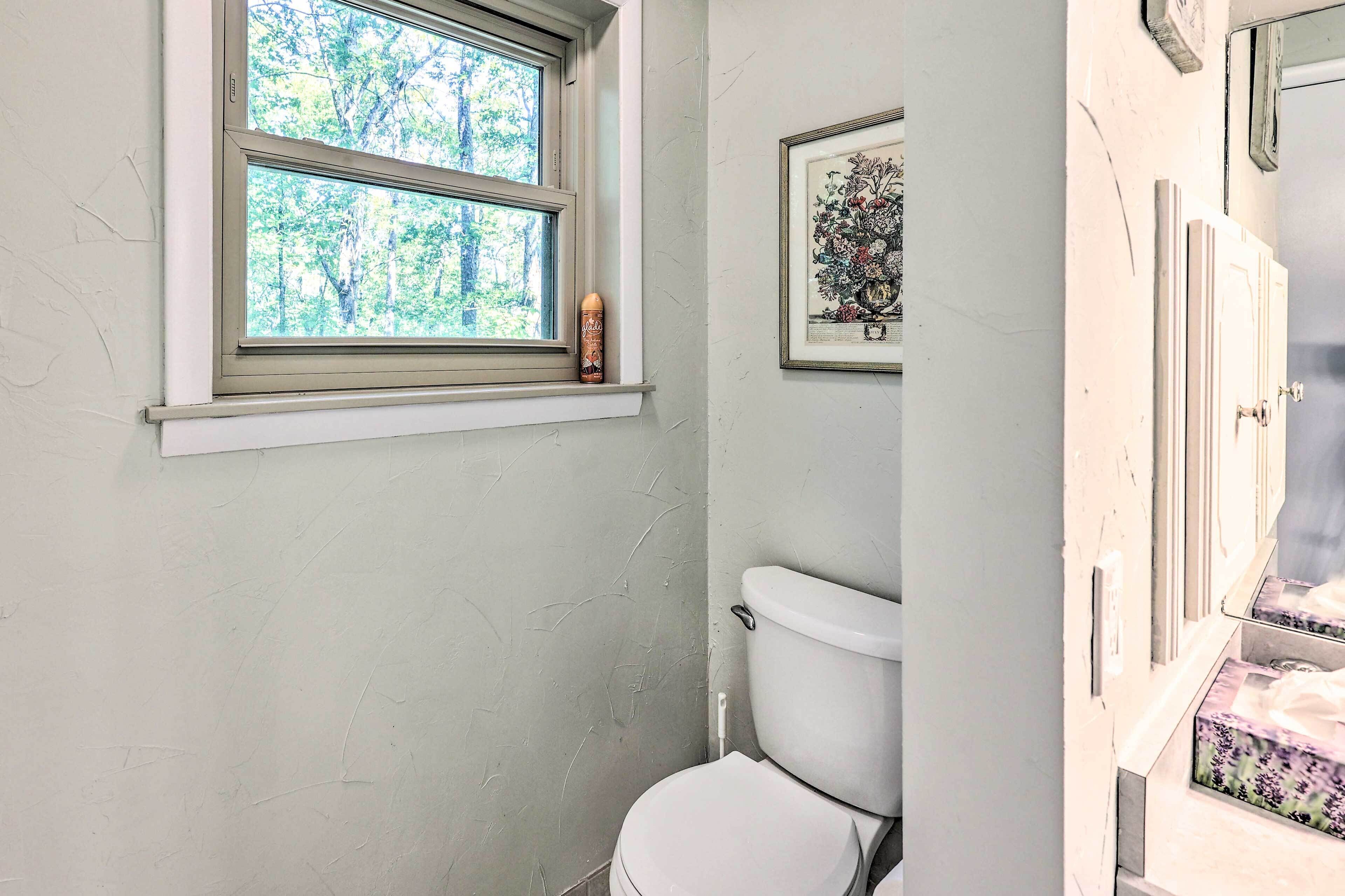 Een badkamer met een raam, toilet en een lijst met een afbeelding aan de muur.