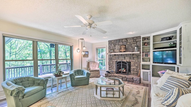 A spacious living room with a fireplace, large windows, and a stone accent wall. - Furnished Deck w/ Views: Hot Springs Cottage (Hot Springs Village)