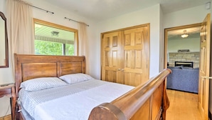 Une chambre avec un lit en bois, une fenêtre avec des rideaux, une armoire en bois et une vue sur une cheminée dans la pièce adjacente.