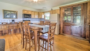 Une cuisine avec des meubles de rangement en bois, une table à manger avec des chaises, un réfrigérateur et un ventilateur de plafond.