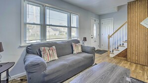 A living room with a grey sofa, striped pillows, a wooden floor, and a staircase with wooden railings. - Middletown Township Home, Close to Beaches! (Leonardo)