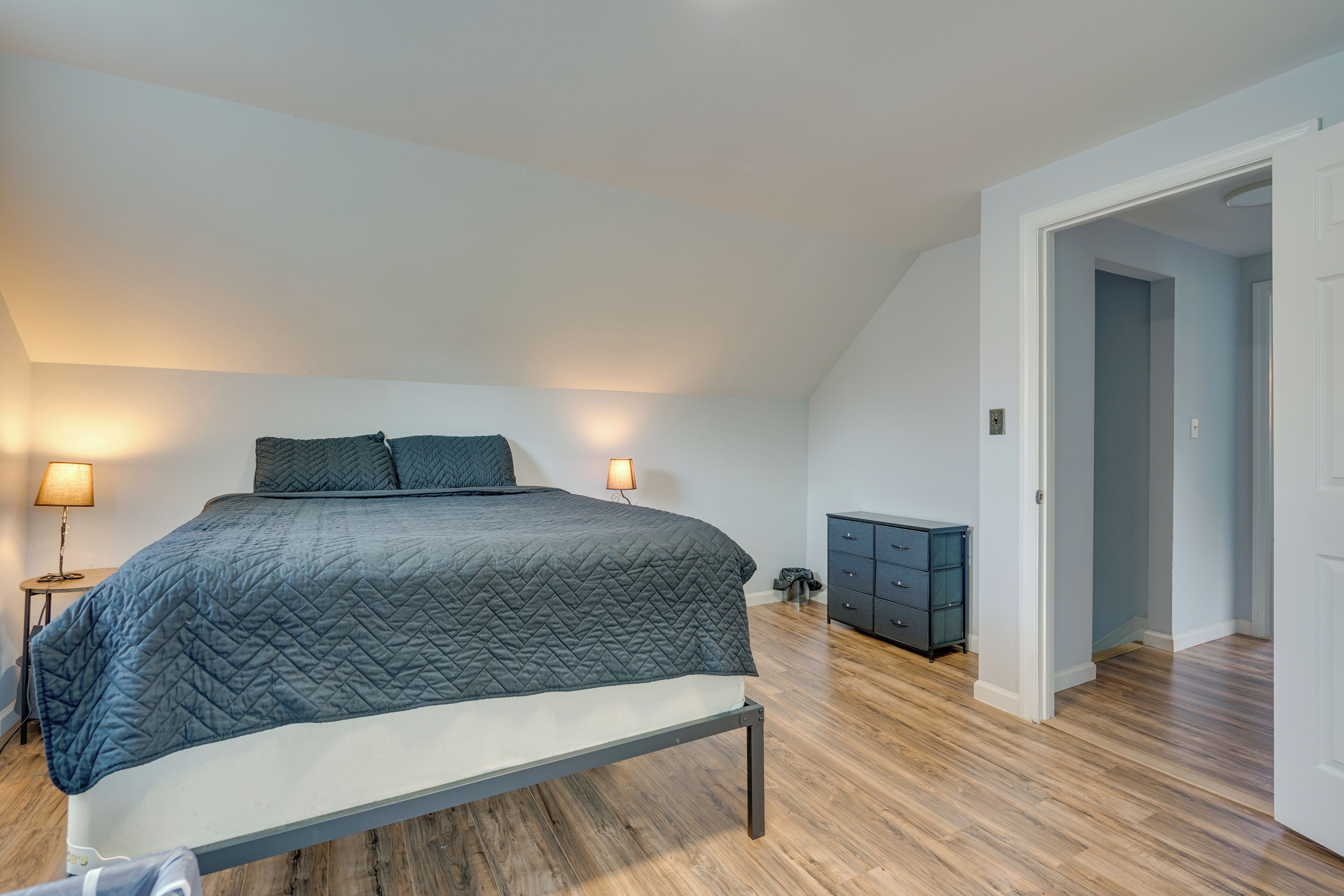 Une chambre à coucher comprenant un lit, des lampes de chevet, une commode et une porte donnant sur une autre pièce.