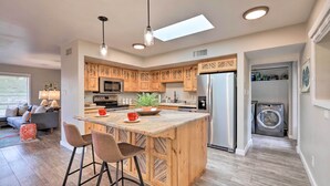 A modern kitchen with wooden cabinets, a central island with bar stools, a built-in oven, and a washing machine in the adjacent room.