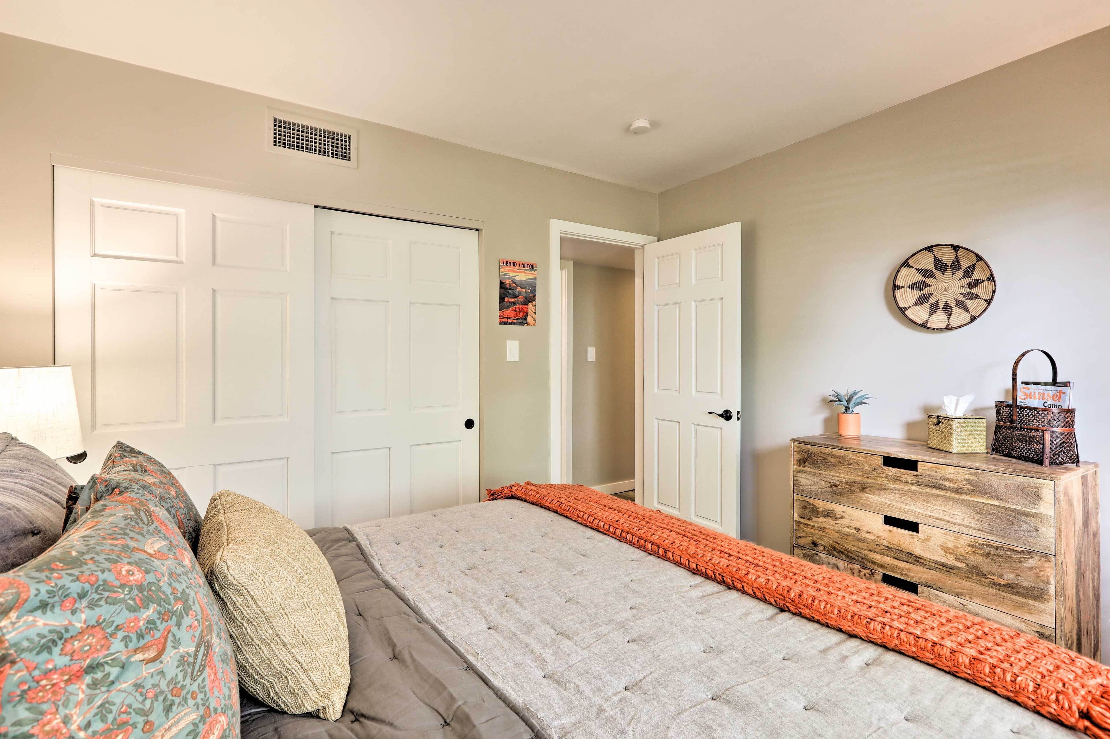A bedroom with a bed, two doors, a dresser, and a wall decoration.