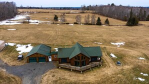 A large, two-story log cabin with a green roof, a covered porch, and a fenced yard.