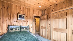A wooden-paneled bedroom with a bed, a door, and a framed picture on the wall.