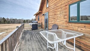 A wooden cabin with a deck, a table, and a grill.