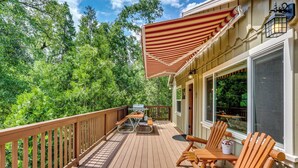 A wooden deck with a picnic table and chairs, a grill, and a large striped awning. - Rustic Oakhurst Retreat < 4 Mi to Bass Lake! (Oakhurst)