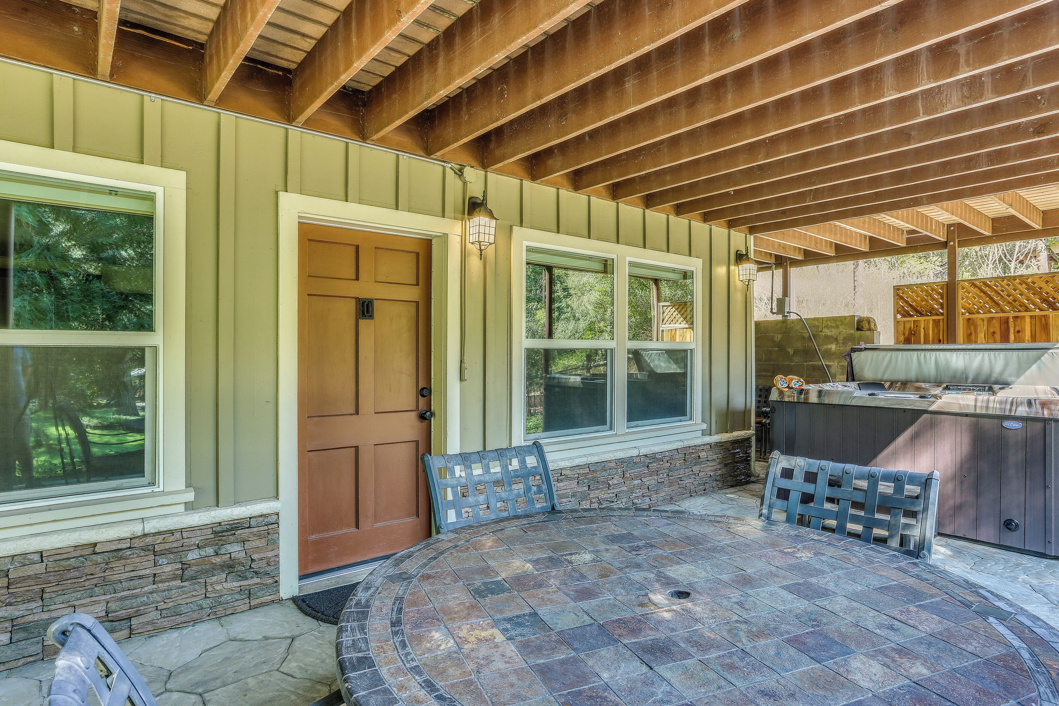 A covered patio with a stone table and benches, a hot tub, and a wooden deck.