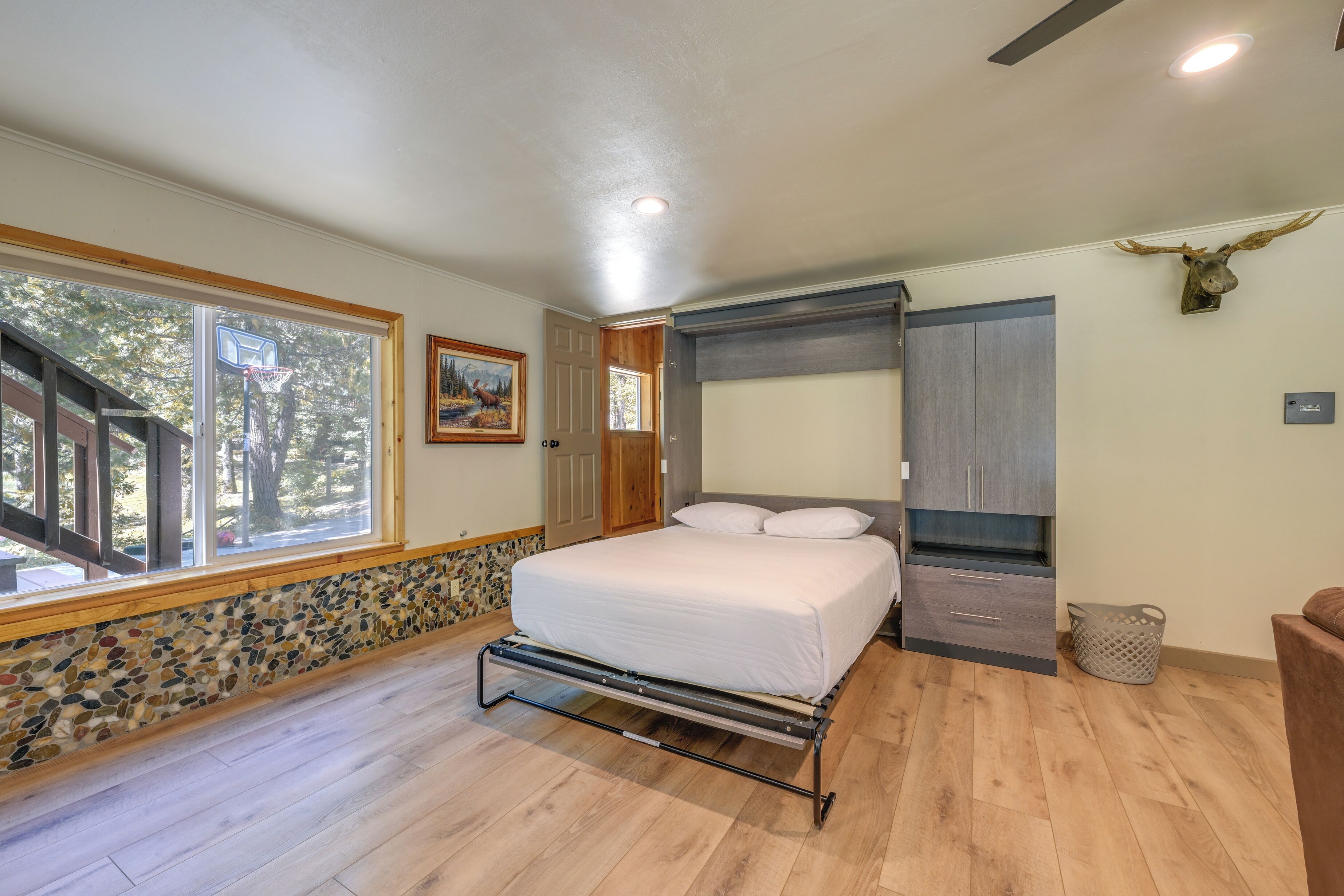 A bedroom with a bed, a window, a door, a wall-mounted cabinet, and a ceiling fan.