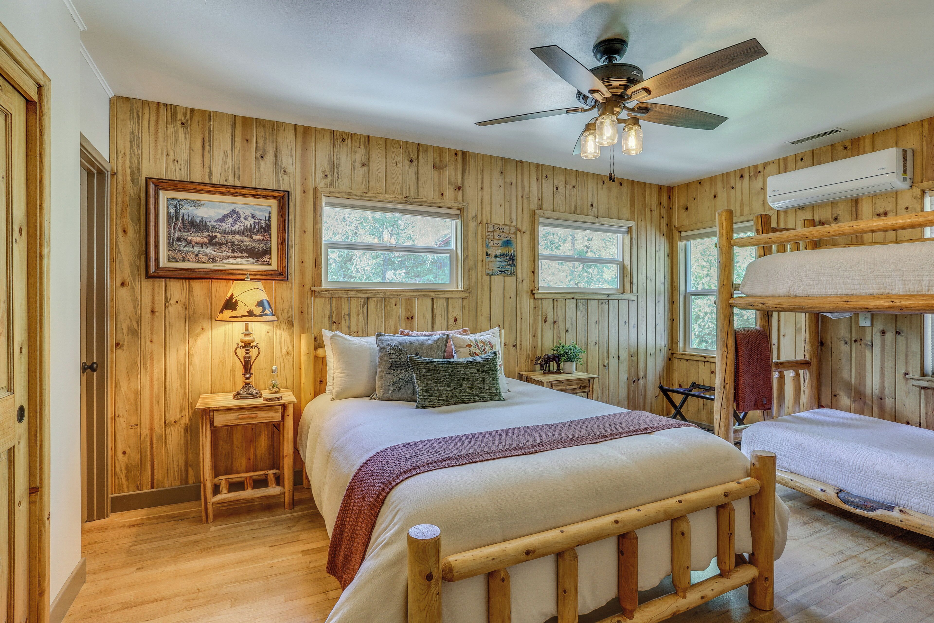 A wooden cabin bedroom with a bed, bedside tables, a ceiling fan, and bunk beds.