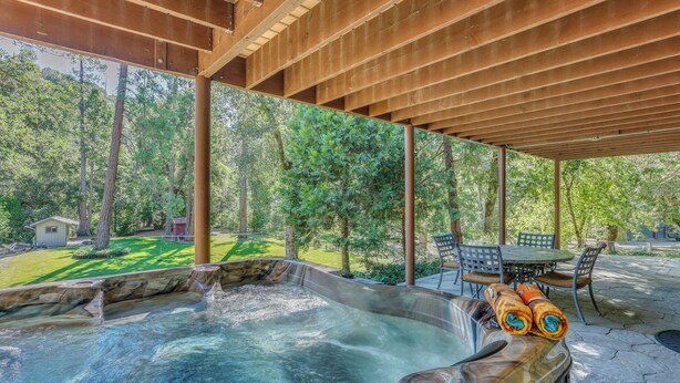 A hot tub area with a wooden pergola, a stone patio, and a view of a green lawn and trees. - Rustic Oakhurst Retreat < 4 Mi to Bass Lake! (Oakhurst)