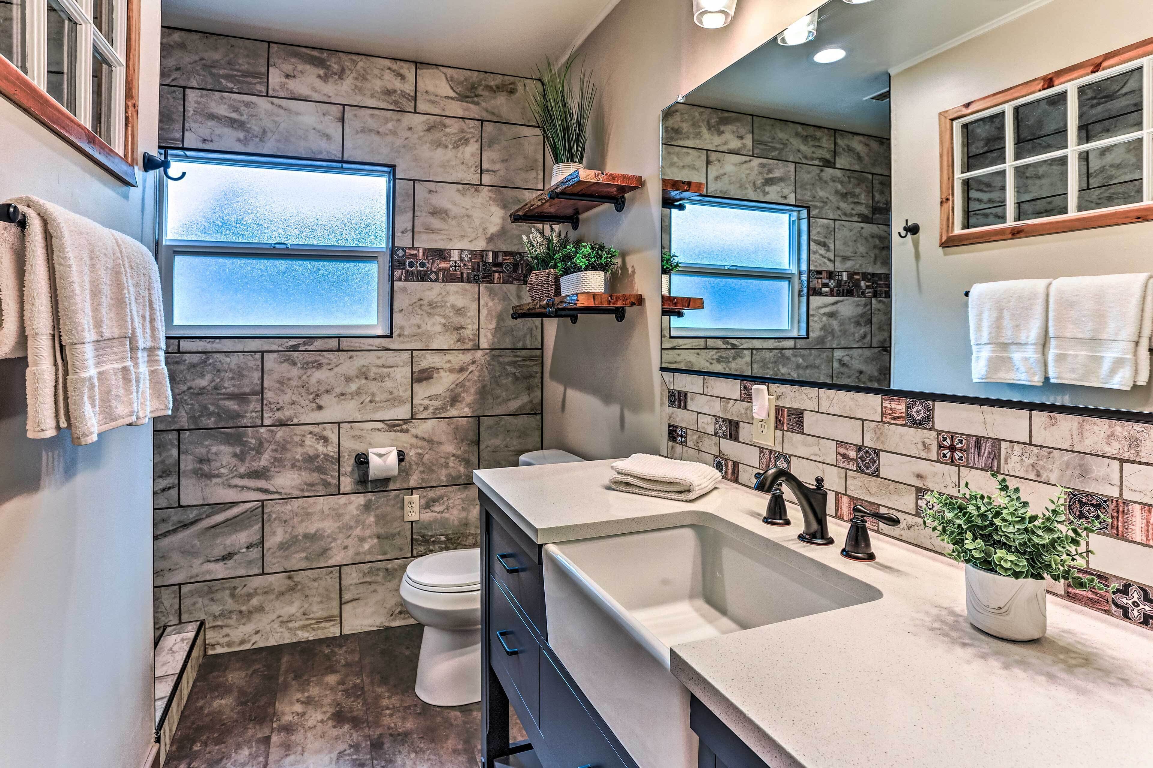 A bathroom with a marble wall, a sink with a mirror, and a toilet.