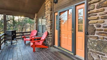 A wooden deck with a stone wall, a sliding glass door, and two red Adirondack chairs.