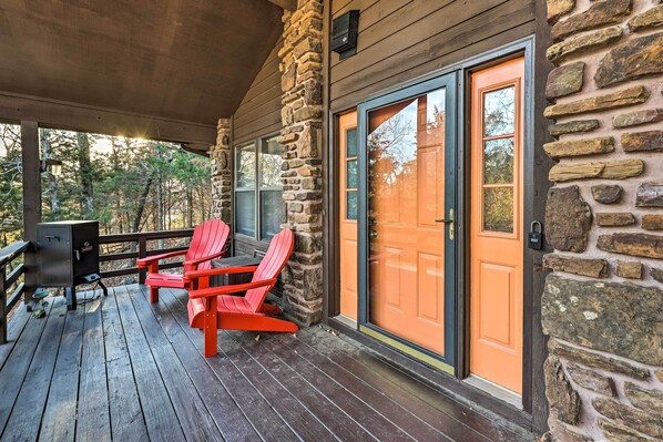 A wooden deck with a stone wall, a sliding glass door, and two red Adirondack chairs.