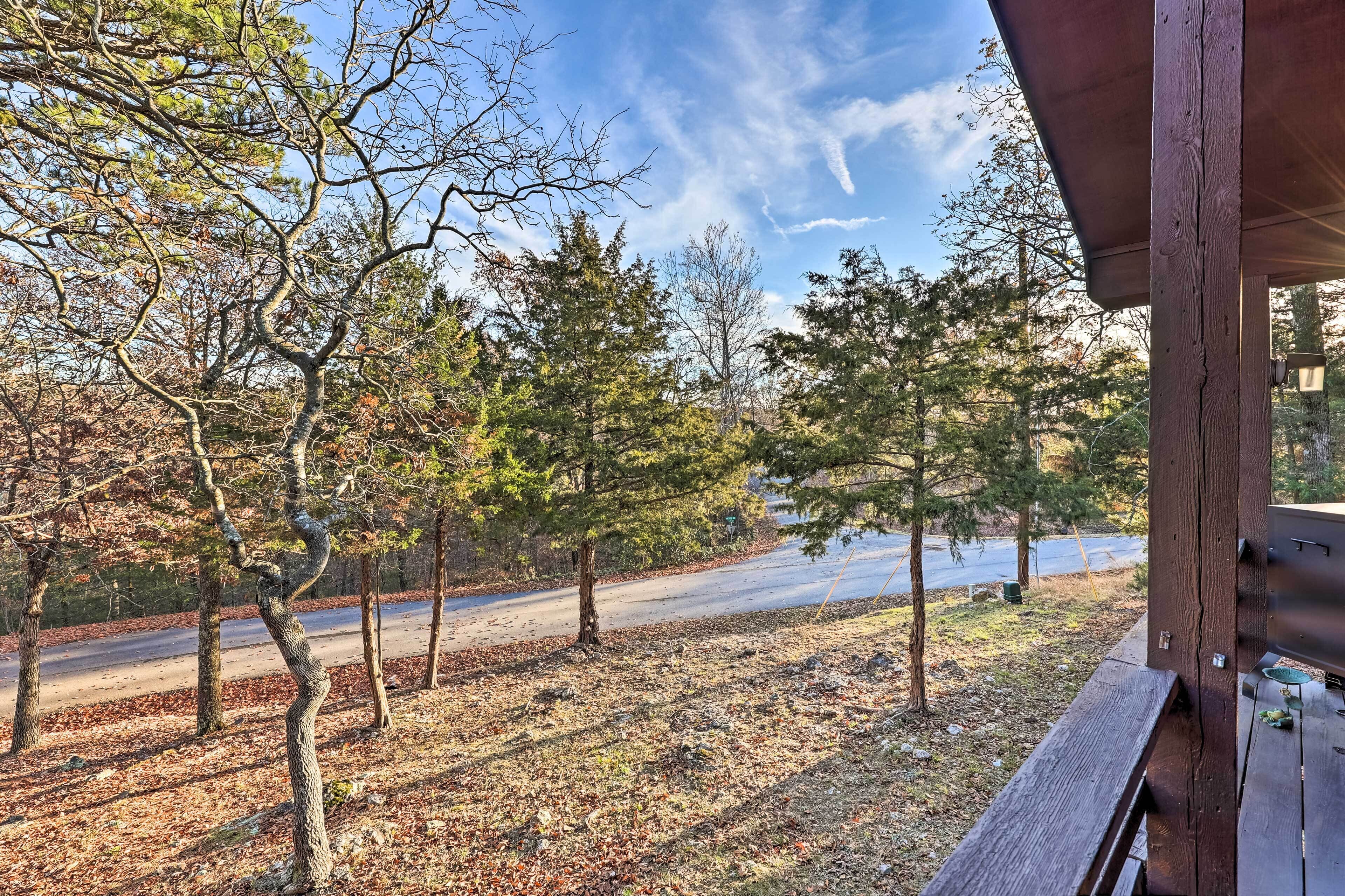 A view from a covered outdoor area with a wooden bench, trees, and a road in the background.