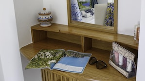 Uma toucador de madeira com um espelho, um vaso de cerâmica decorativo, uma revista e uma necessaire de produtos para a pele.