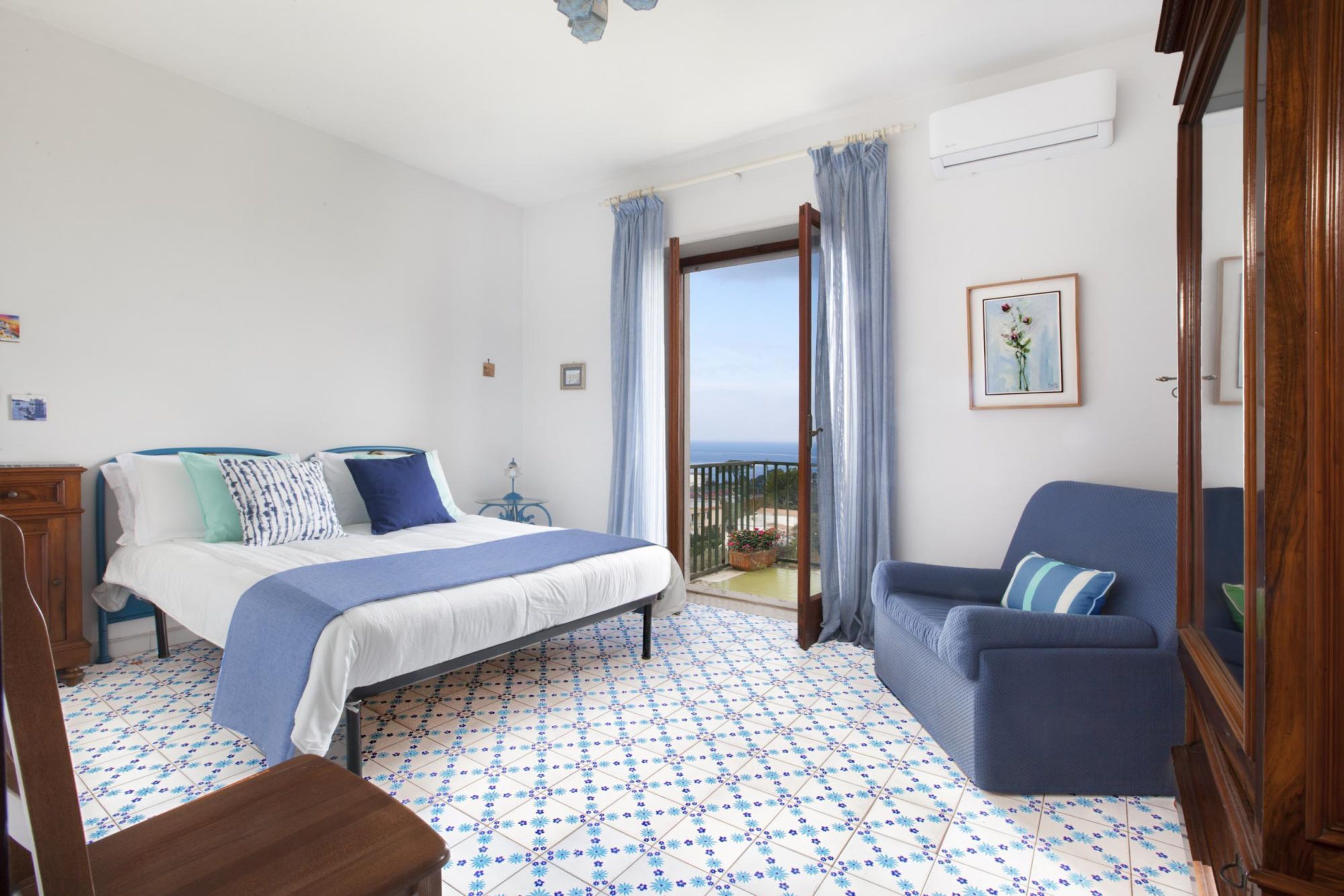 A hotel room with a bed, a sofa, a balcony with a view, and a tiled floor.