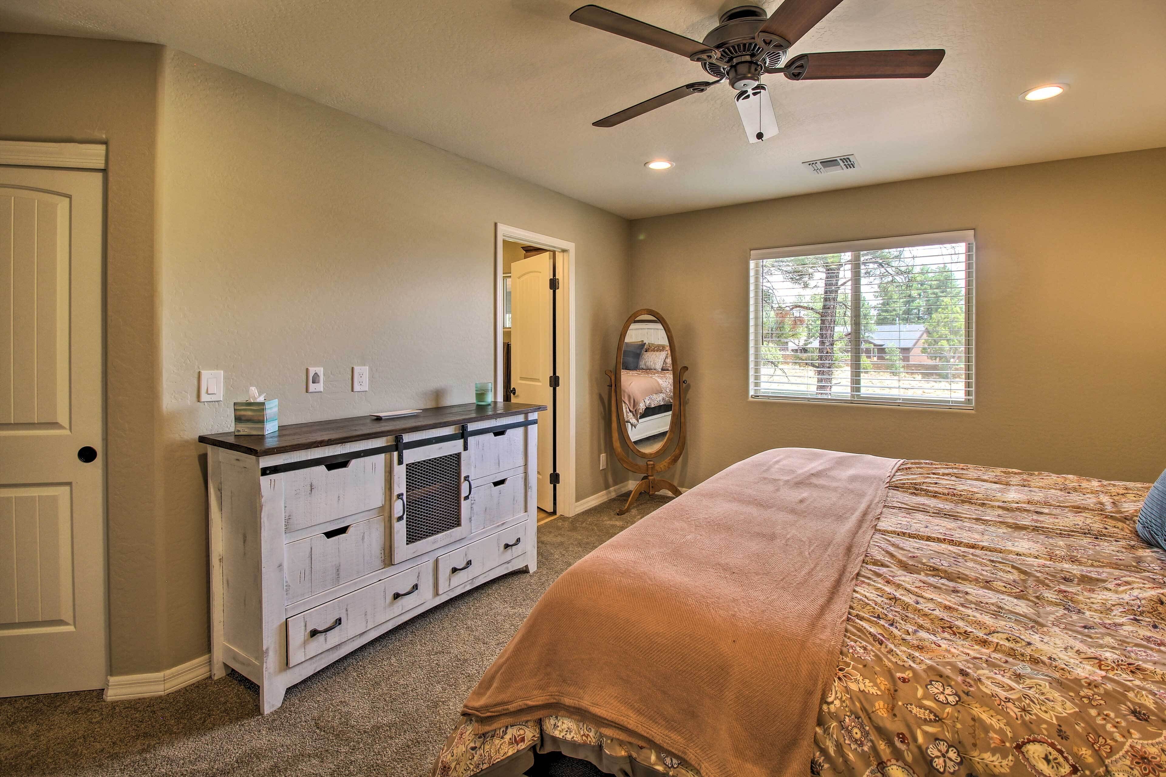 A bedroom with a bed, a dresser, a ceiling fan, a window, and a door.