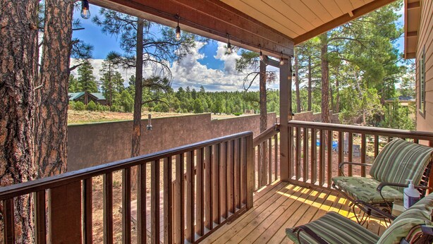 A wooden deck with a railing, two chairs, and a view of a forested area.