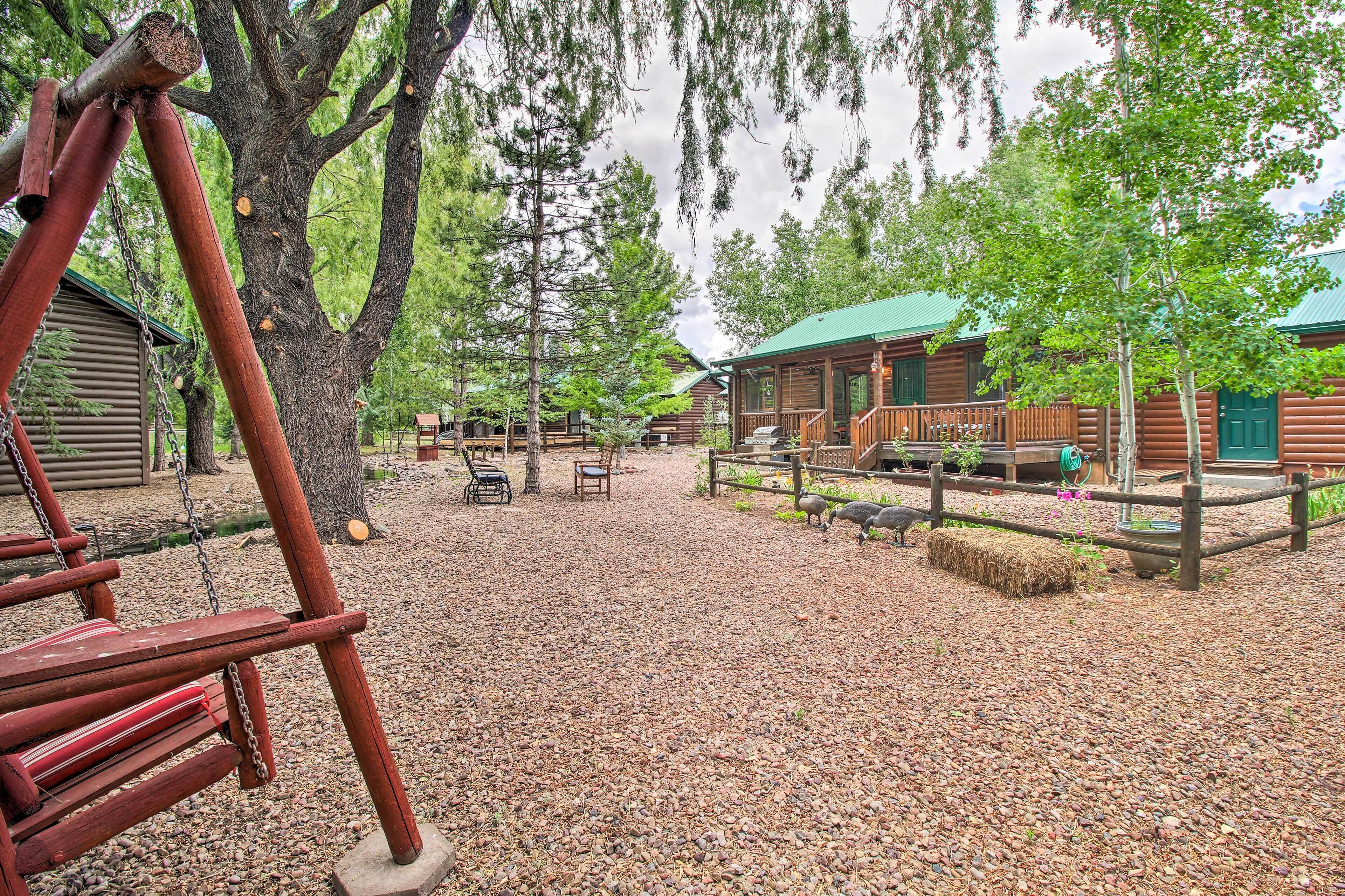 A rustic cabin with a green roof, surrounded by trees and a gravel path.